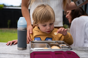 Child eating crackers out of leak proof stainless steel lunch box on a table 